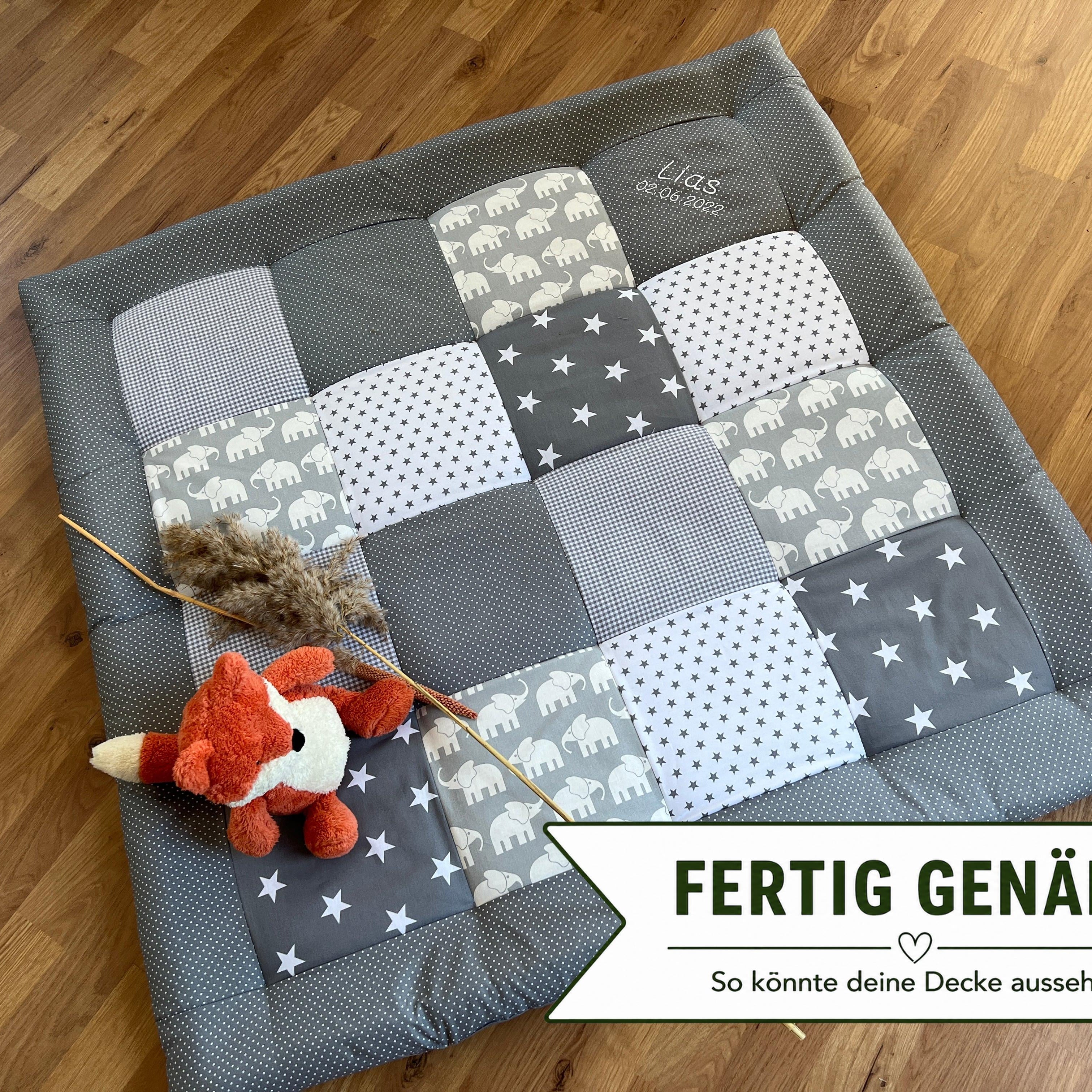 A gray and white patchwork quilt with a stuffed animal fox is placed on a wooden floor.