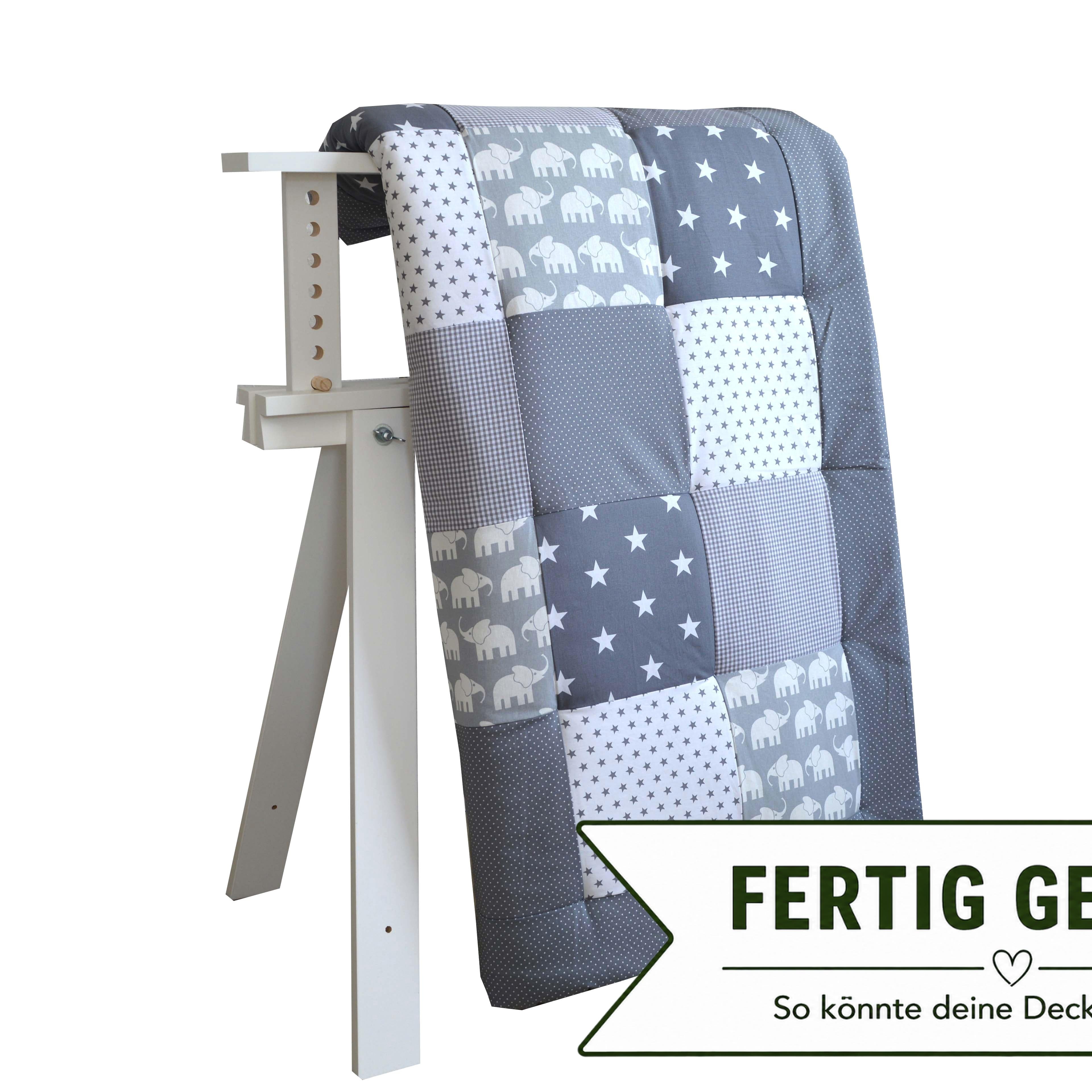 A gray and white patchwork quilt is displayed on a white wooden stand against a white background.