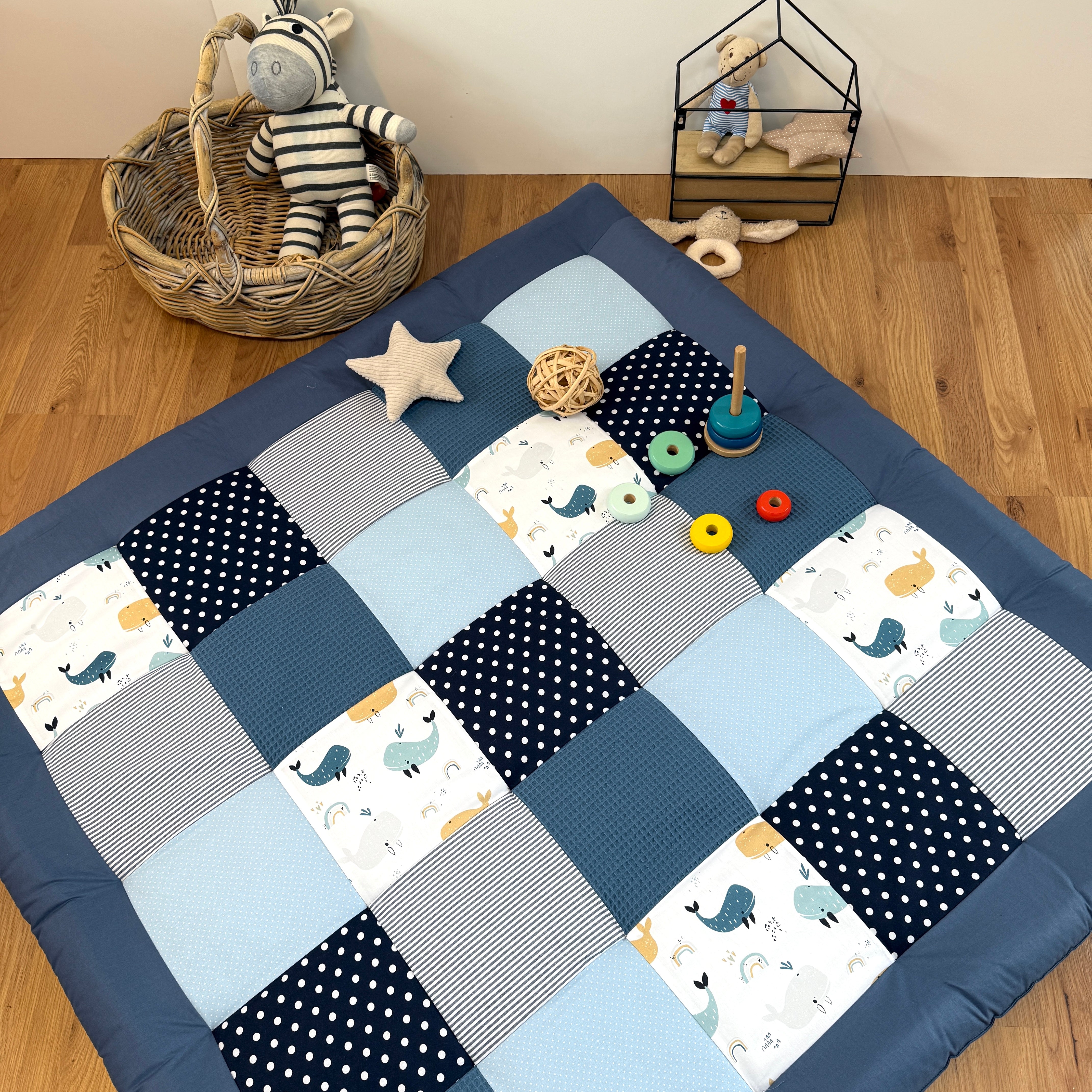 A blue and white quilt with a star pattern, a basket with a stuffed animal, and various toys on a wooden floor.