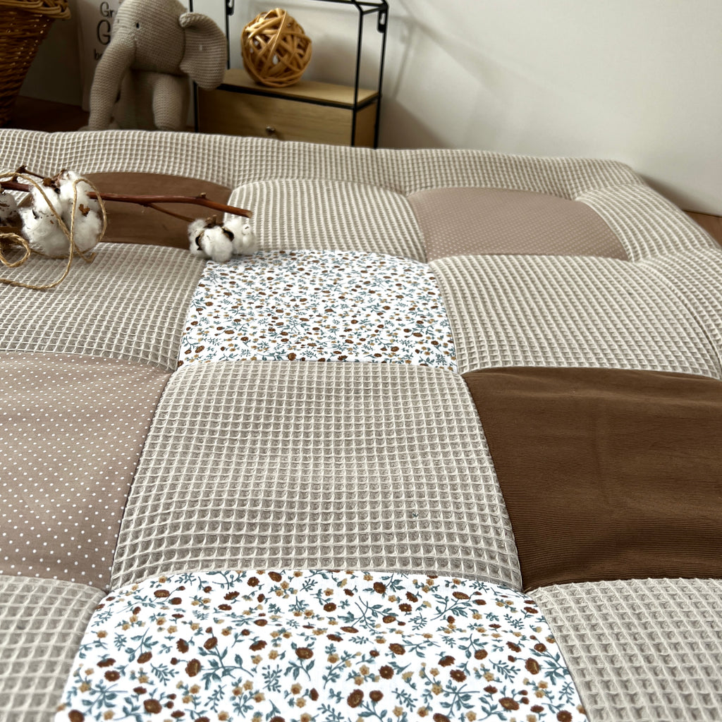 a close-up view of a bed with a patchwork quilt, featuring a variety of textures and patterns. The quilt is composed of several square pieces, each with a different design, creating a visually interesting and cozy appearance.