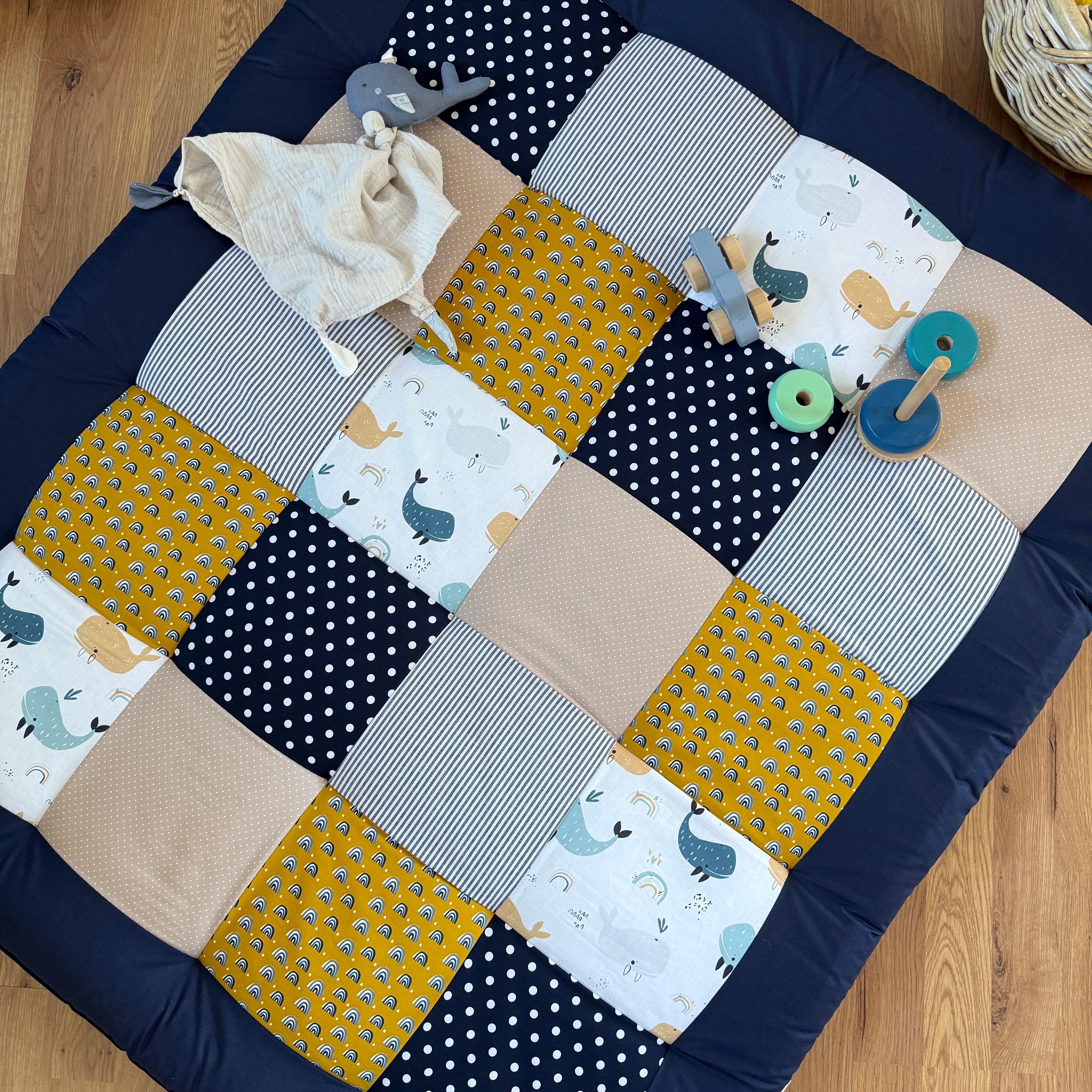 A handmade quilt with a patchwork design of various colors and patterns, including polka dots, stripes, and animal prints, laid out on a wooden floor.