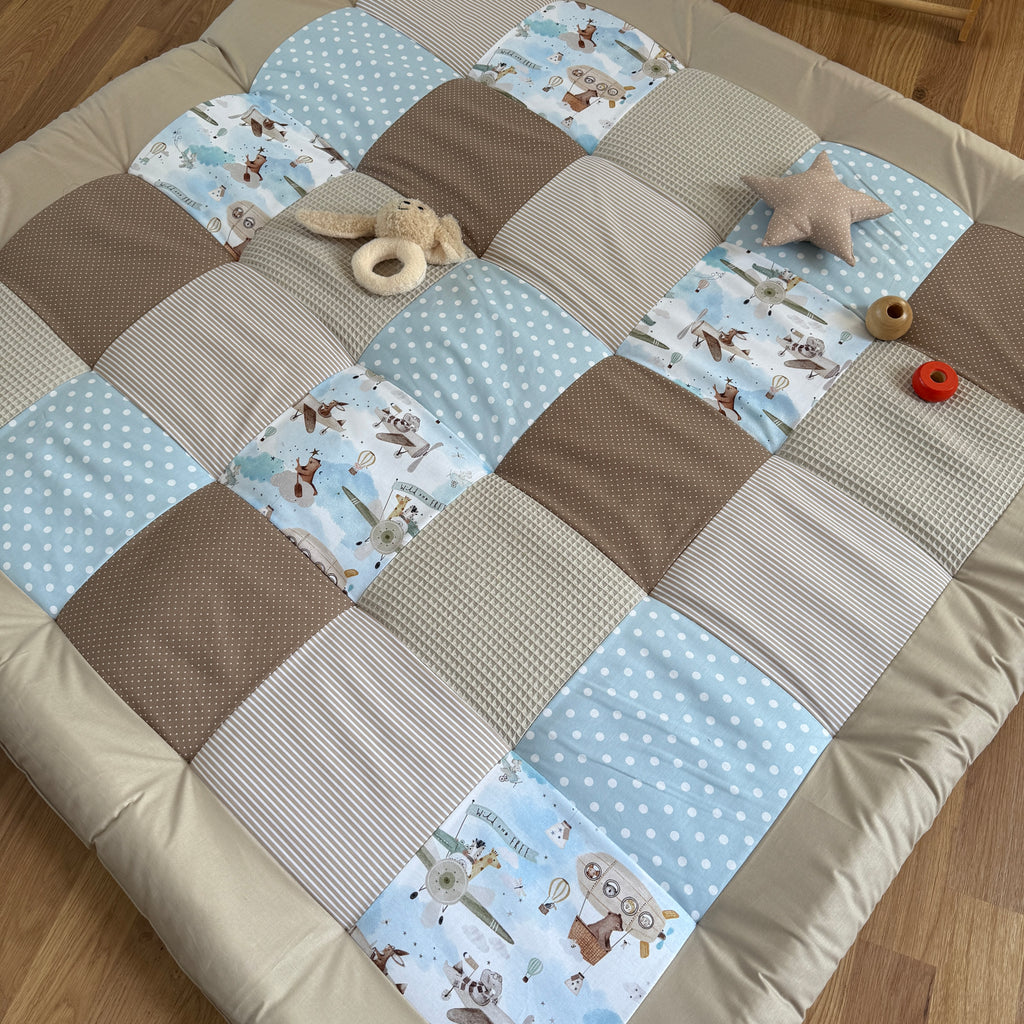 A patchwork quilt with various patterns and textures, including polka dots, stripes, and animal prints, is spread out on a wooden floor. There are also some toys and a star-shaped object placed on the quilt.