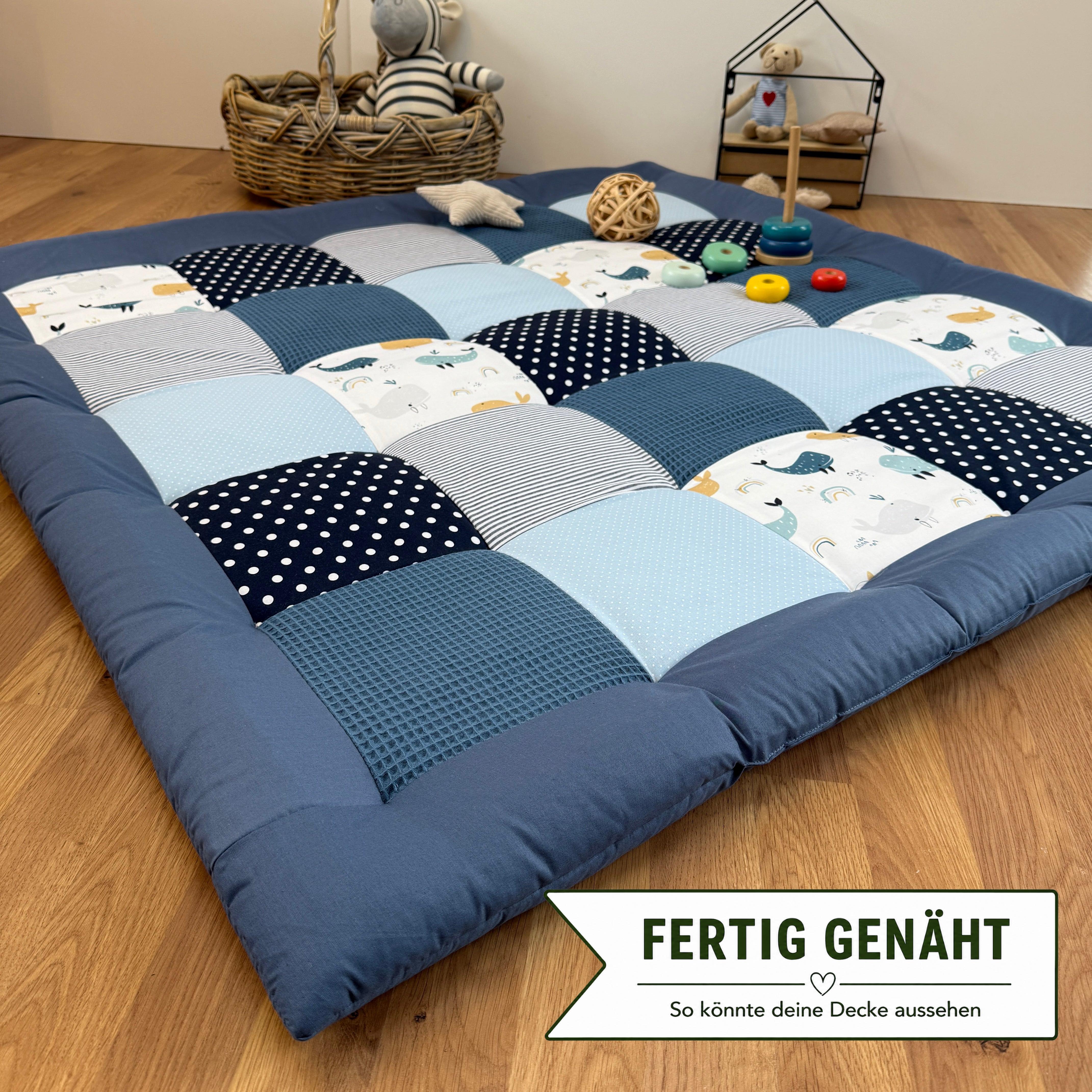 A blue and white quilt-like bedspread with a checkered pattern, placed on a wooden floor. The bedspread has various geometric patterns and polka dots. There are also some toys and a basket in the background.