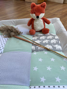A red stuffed fox toy sits atop a quilt with a blue and white striped pattern and white stars.
