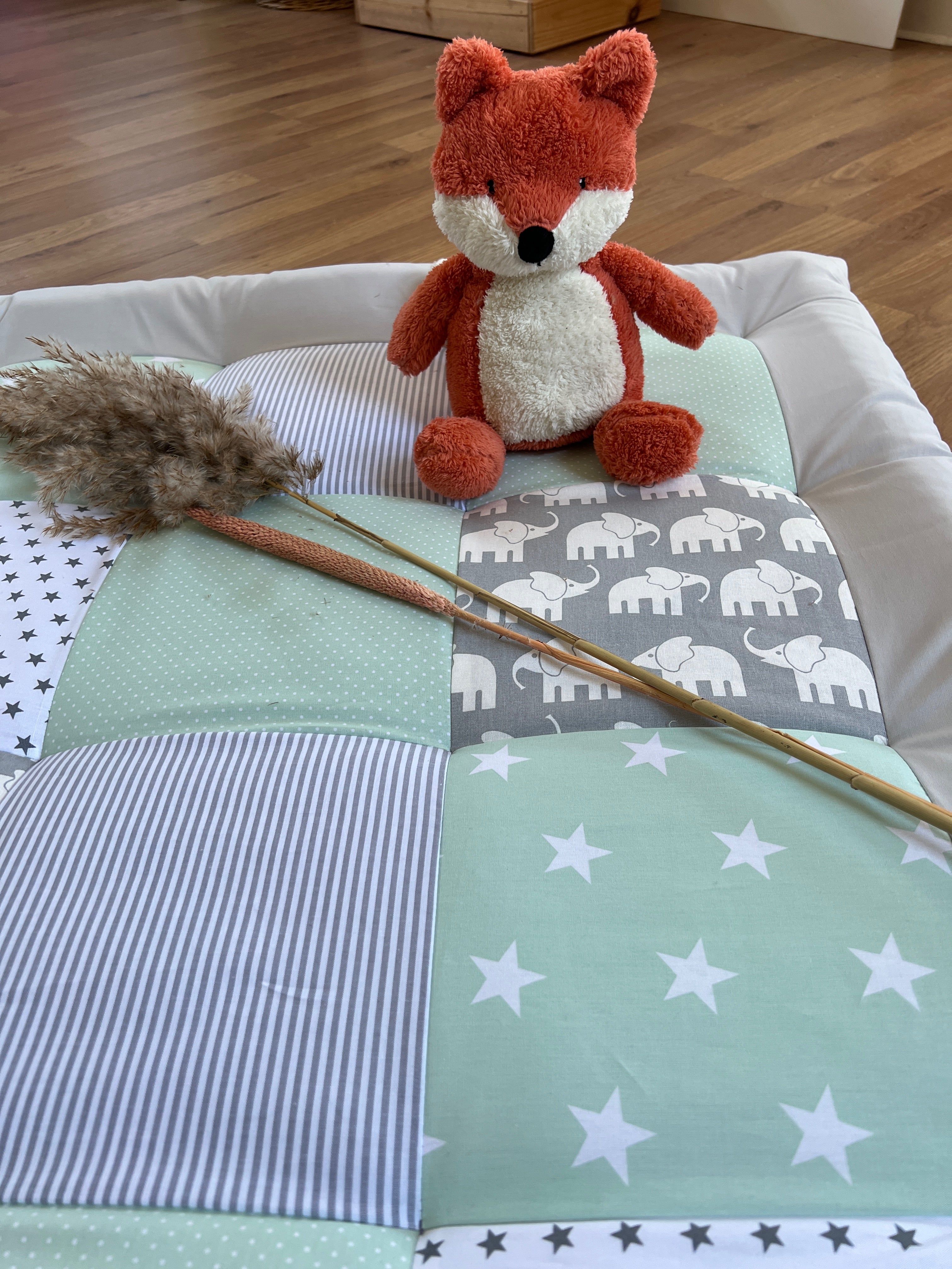 A red stuffed fox toy sits atop a quilt with a blue and white striped pattern and white stars.