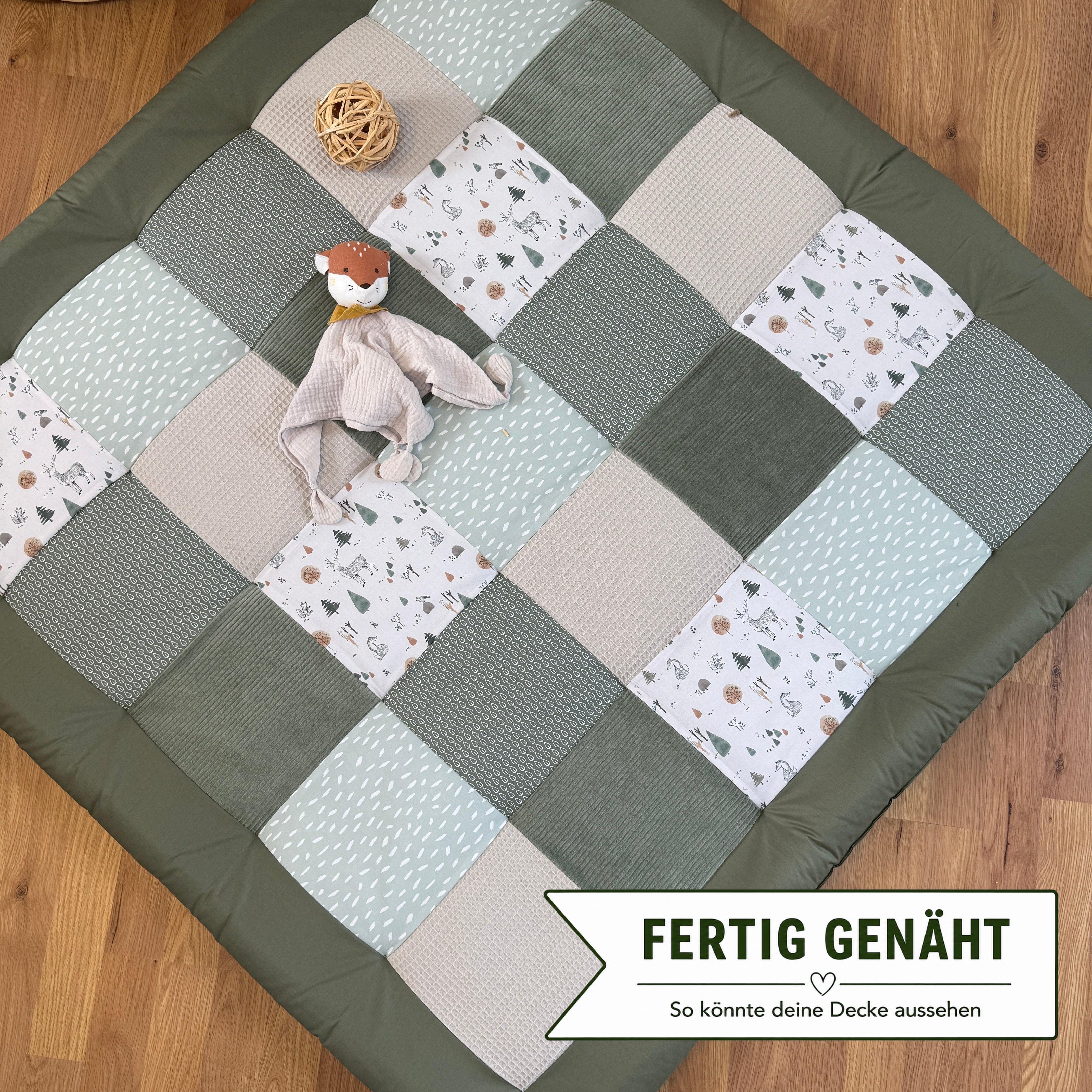 A handmade patchwork quilt with various patterns and textures, including a small stuffed animal toy, is spread out on a wooden floor.