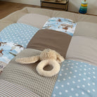 A stuffed animal toy, specifically a teddy bear, is placed on a bed with a patchwork quilt featuring various patterns and colors.