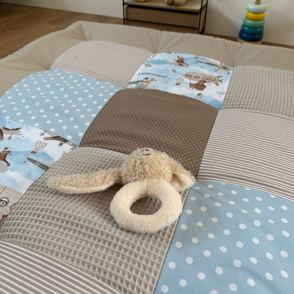 A stuffed animal toy, specifically a teddy bear, is placed on a bed with a patchwork quilt featuring various patterns and colors.