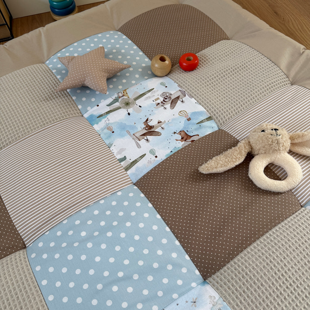 a patchwork quilt with various textures and patterns, including a star-shaped pillow, a stuffed animal, and a toy airplane.